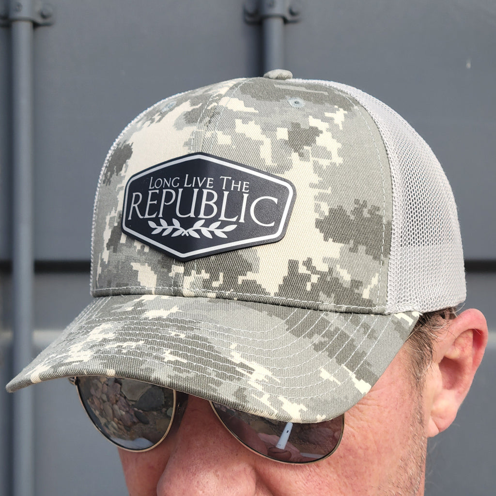Camouflage cap with 'Long Live The Republic' logo held by a person against a gray background